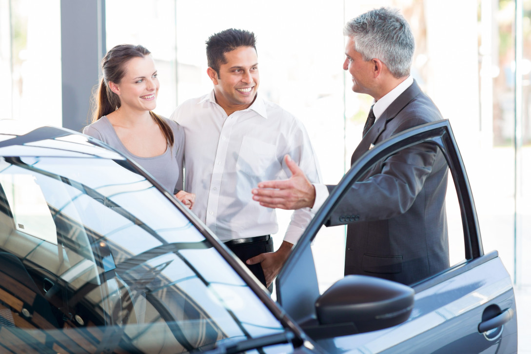 mature salesman showing new car to a couple